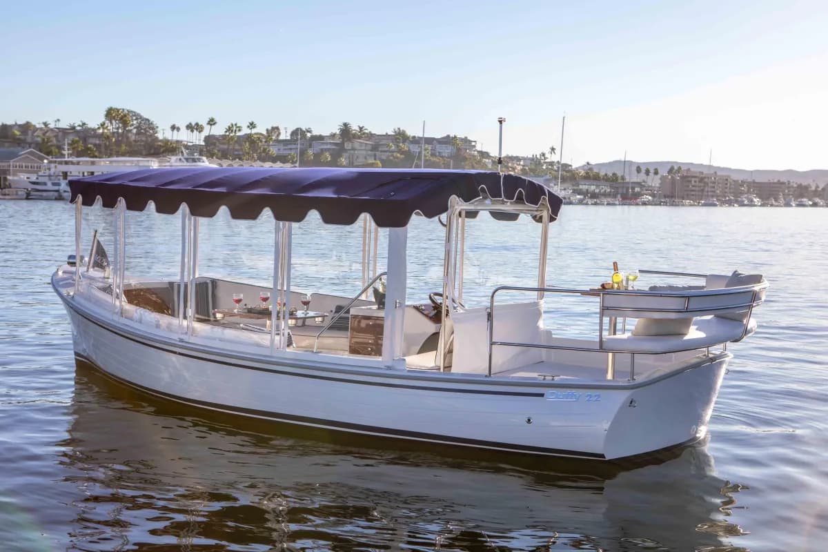 An elegant standard white Duffy boat with a navy canopy on Alamitos Bay at golden hour
